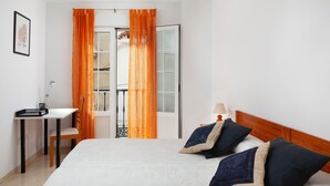 Una habitación de hotel con cama, escritorio, silla y ventana con cortinas.
