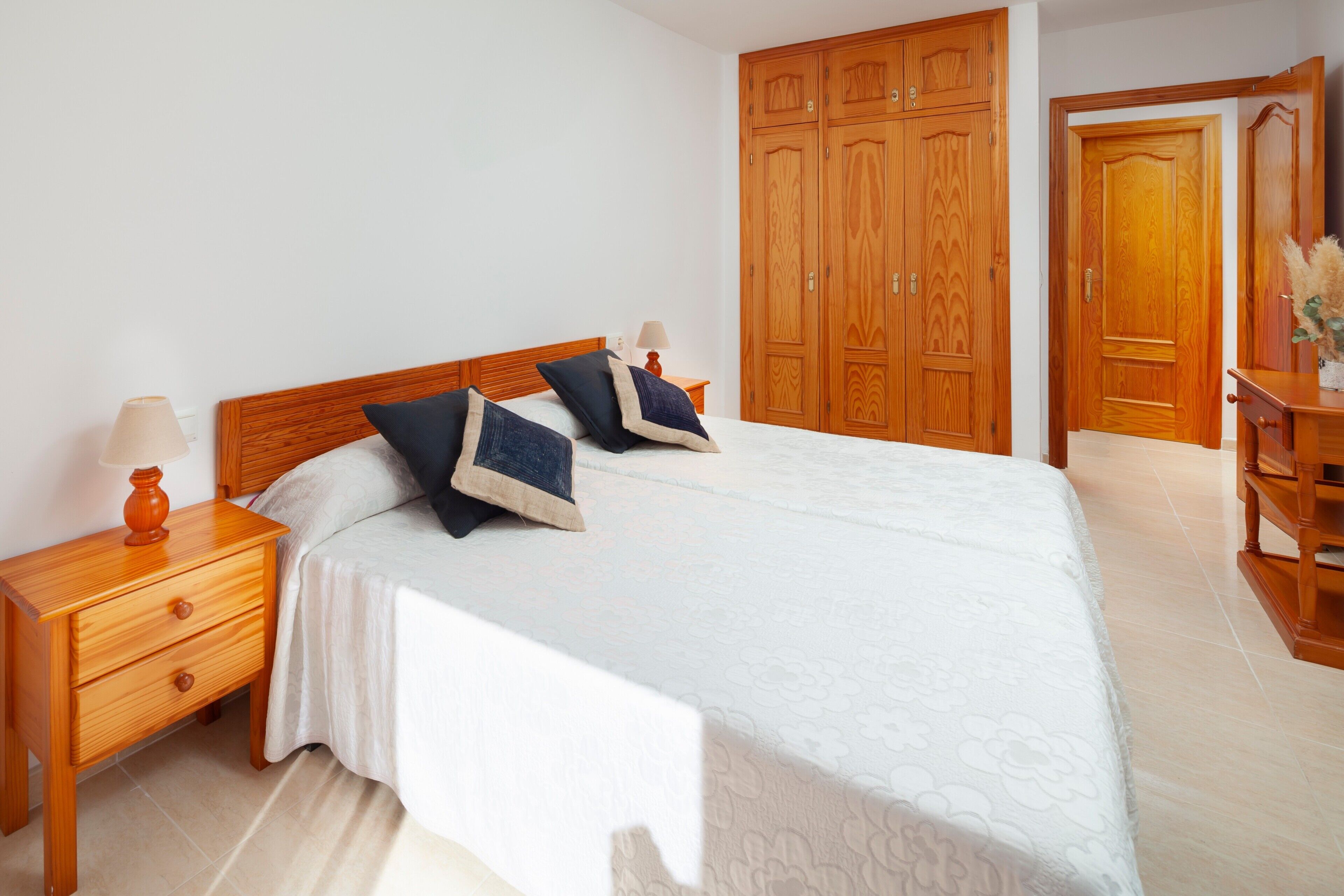 A bedroom with a bed, wooden wardrobe, nightstand, and lamp.