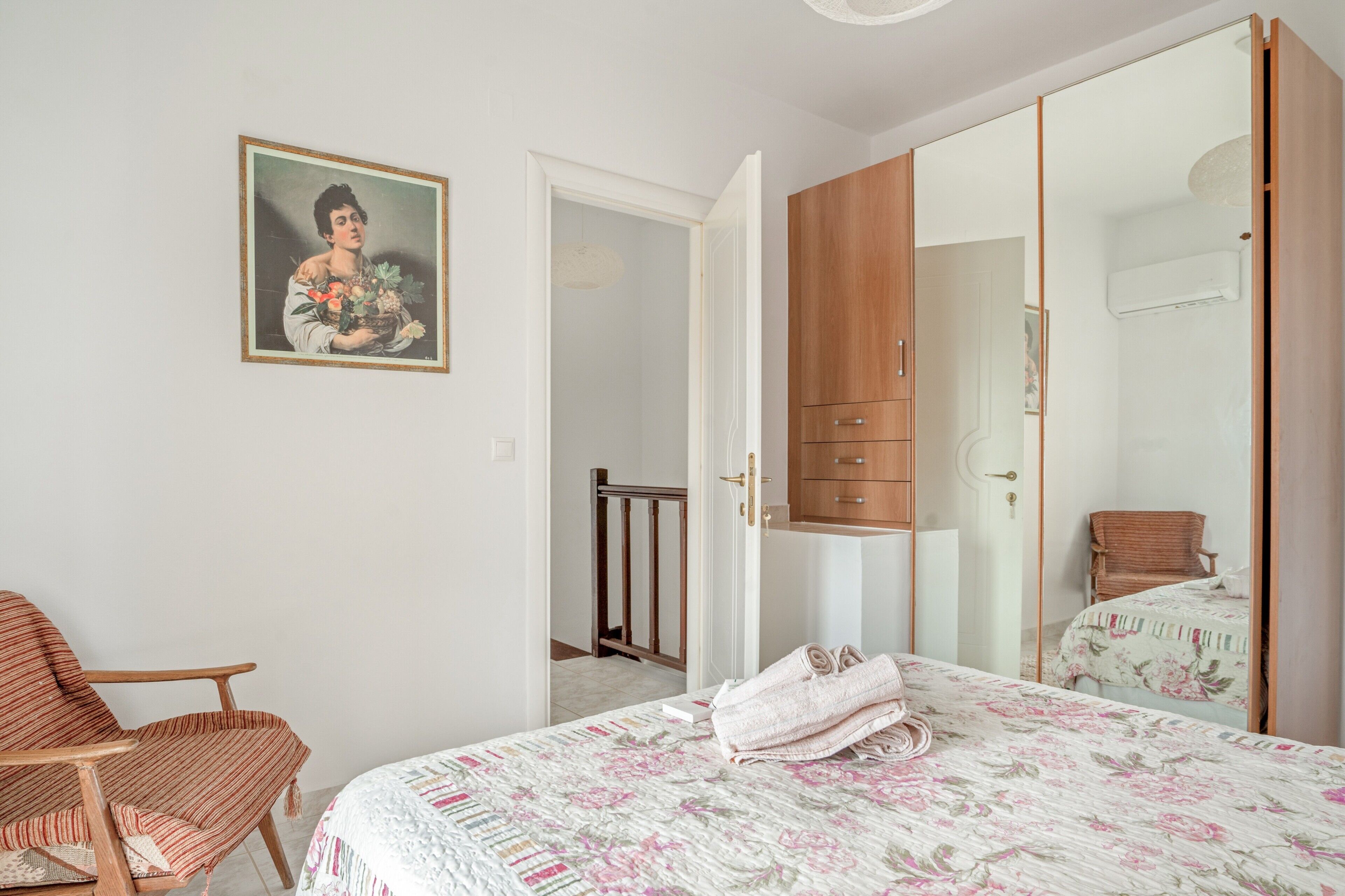 A bedroom with a bed, a chair, a wardrobe, and a painting on the wall.