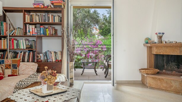Ein gemütliches Wohnzimmer mit Bücherregal, Kamin und Blick auf einen Balkon mit Blumen.