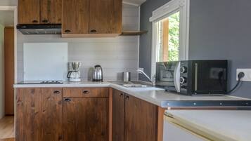Une cuisine compacte dotée de meubles en bois, d’une cuisinière, d’une machine à café, d’une bouilloire, d’un four à micro-ondes et d’un évier.