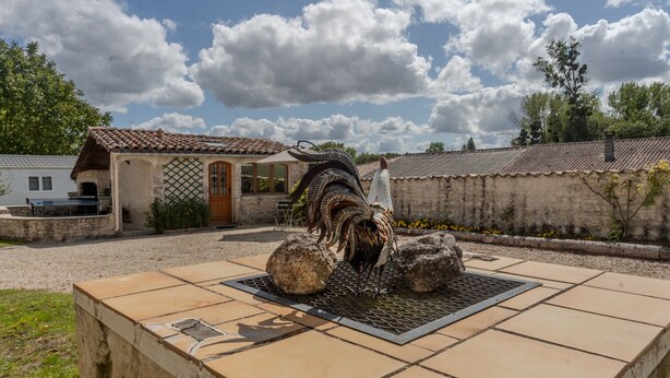 A courtyard with a decorative metal sculpture, a stone bench, and a building with a tiled roof. - Maison 'Les Roses De Jonzac' with Private Pool, Private Terrace, and Wi-Fi (Mortiers)