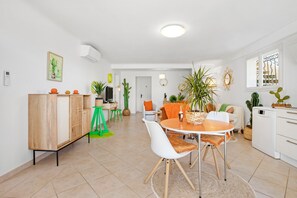Un salon moderne avec un coin repas, comprenant un meuble en bois, des chaises blanches, une table ronde et diverses plantes en pot.