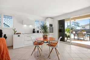 A modern kitchen with white cabinets, a dining table with two chairs, and a view of the outdoor patio.