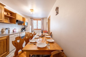 A kitchen with wooden cabinets, a dining table set for six, and a window with curtains.