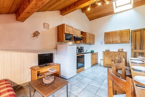 Una cucina compatta con mobili in legno, un forno a microonde, un frigorifero e un'area pranzo con sedie e tavolo in legno.