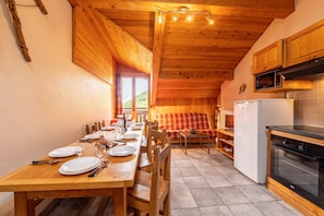 Un tavolo da pranzo in legno apparecchiato con piatti e posate, un divano, una cucina con piano cottura e forno a microonde, e una finestra con vista.