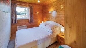 A wooden cabin bedroom with a bed, a window with curtains, and wall-mounted lights.