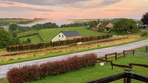 A rural landscape with a road, a stone house, and a lake in the background.