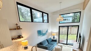 A modern kitchen with a central island, white cabinetry, and a large window overlooking a backyard.
