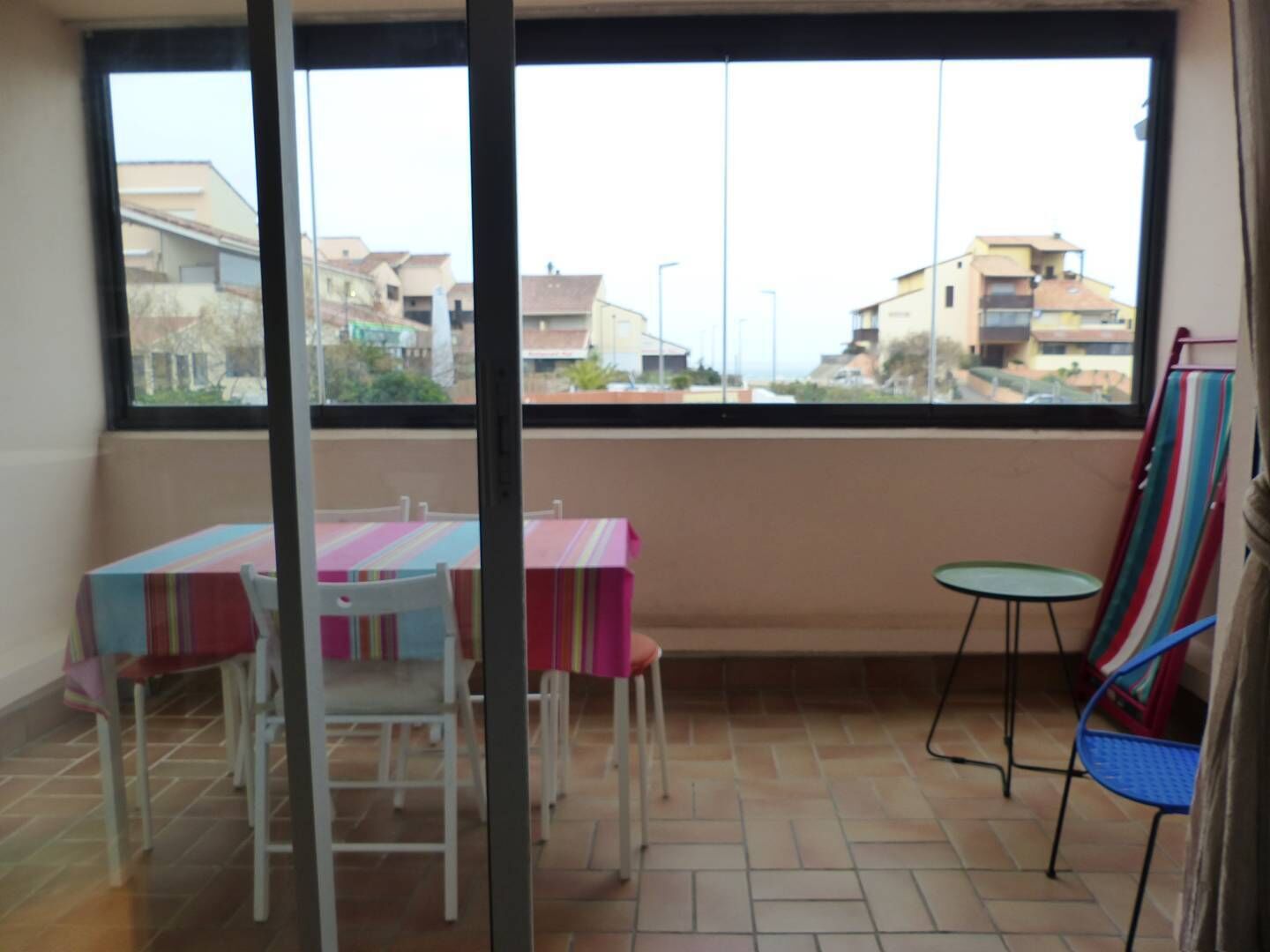 A balcony with a table and chairs, a small table, and a striped chair.