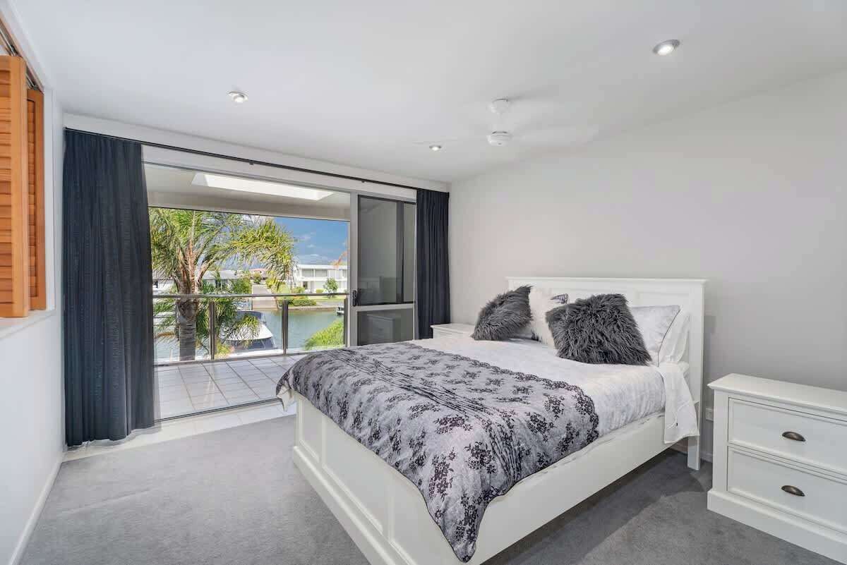 A bedroom with a large bed, a nightstand, a sliding glass door leading to a balcony, and a view of the outdoors.