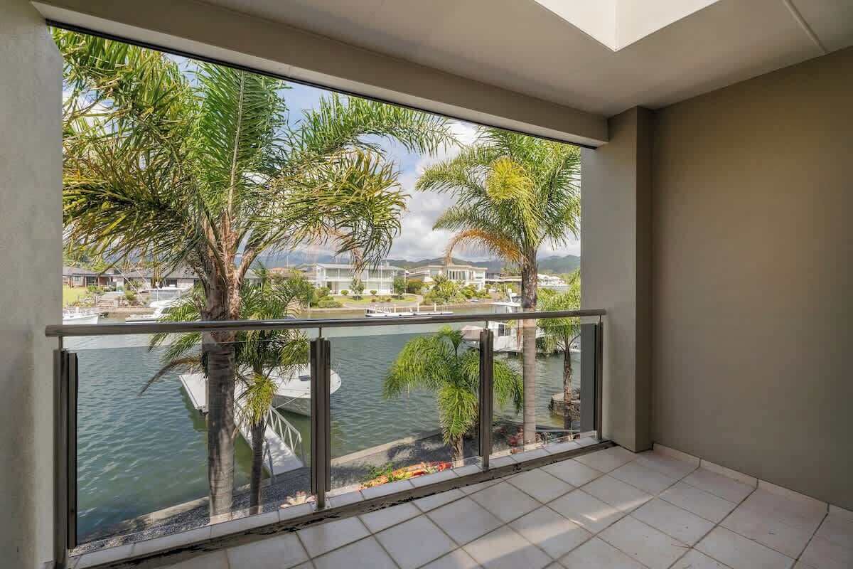 A balcony with a view of a body of water, palm trees, and distant buildings.