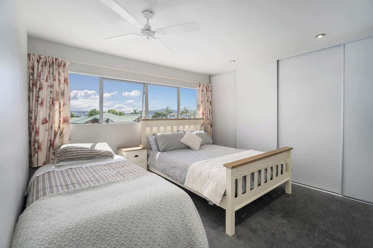 A bedroom with two beds, a ceiling fan, a window with curtains, and a wardrobe.