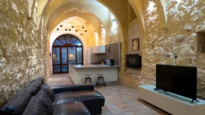 A cozy interior with a stone wall, a leather sofa, a kitchen area, and a flat-screen TV. - Mixel Holiday Home 4 bedrooms with private pool (Ta' Sannat)