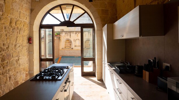 A kitchen with a stone wall, a gas stove, cabinets, and a view through an arched doorway. - Mixel Holiday Home 4 bedrooms with private pool (Ta' Sannat)