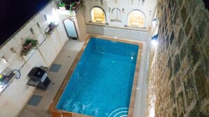 An indoor swimming pool with a stone wall and arched windows, surrounded by lounge chairs and a barbecue grill. - Mixel Holiday Home 4 bedrooms with private pool (Ta' Sannat)