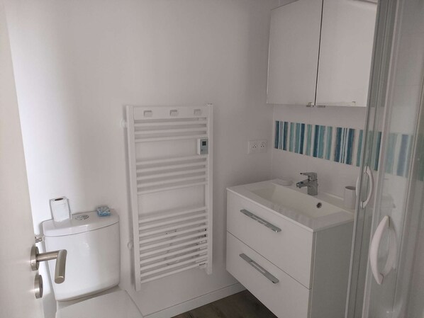 A small, white bathroom with a toilet, a white sink with a mirror, and a white cabinet above the sink.