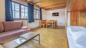 A cozy room with a wooden ceiling, a sofa, a dining table with chairs, and a bed.
