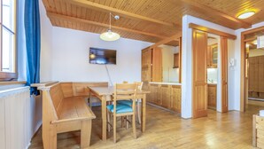 A wooden dining area with a bench and table, a television mounted on the wall, and wooden cabinets in the background.
