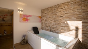 Une salle de bain moderne avec un mur en pierre, une baignoire et un luminaire fixé au mur.