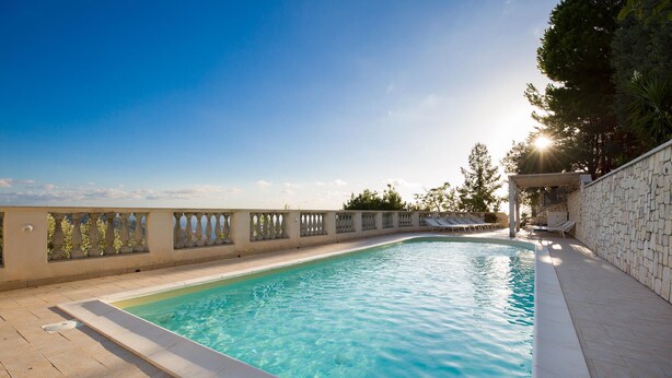 Une piscine avec un mur en pierre et une pergola d’un côté.