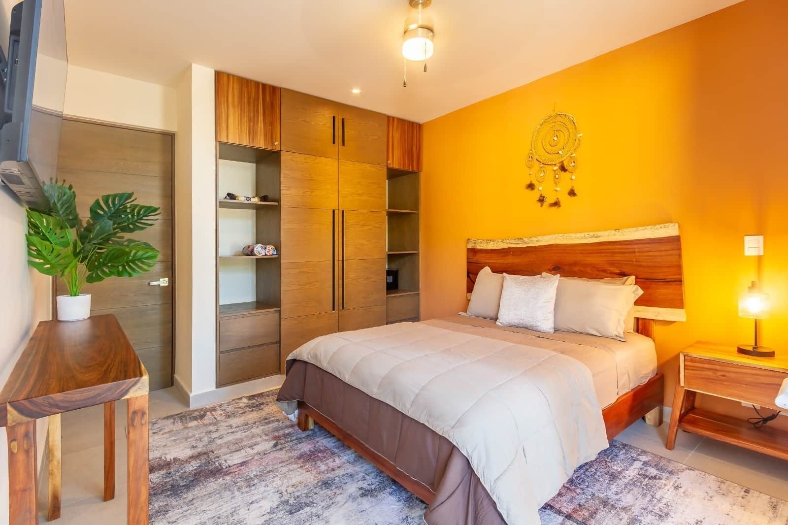 A bedroom with a bed, bedside table, nightstand, wardrobe, and a potted plant.