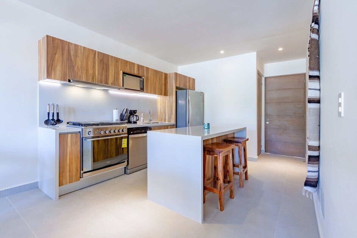 A modern kitchen with a central island, wooden cabinetry, stainless steel appliances, and bar stools.