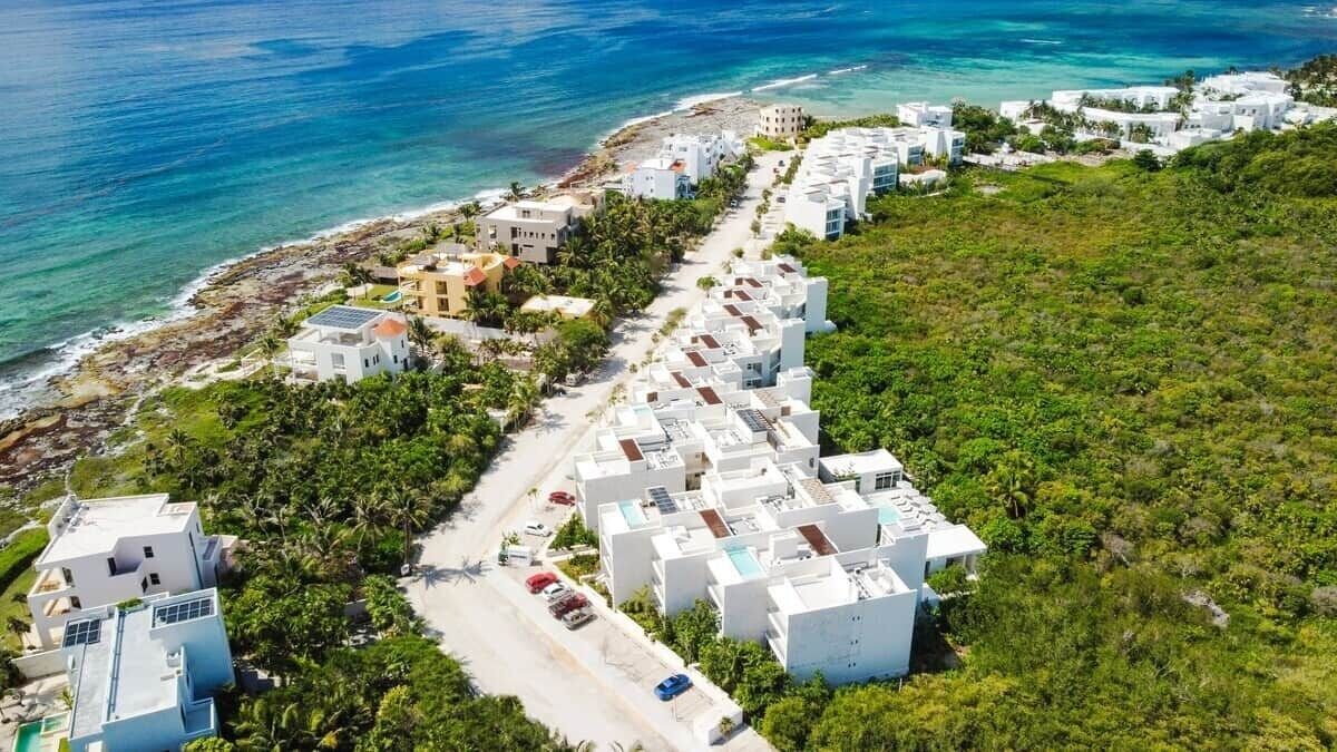 A coastal residential area with white buildings, a beach, and a clear view of the ocean.