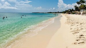 Een strand met helder turquoise water, een zandstrand en enkele mensen die zwemmen.