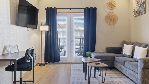 A modern living room with a sofa, a dining table, and a TV mounted on the wall. - European Village King Suite Retreat: Unwind, Explore, Beach, Work! (Palm Coast)