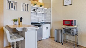 A compact kitchen with white cabinets, a microwave, a toaster oven, and a small dining area with a bench. - European Village King Suite Retreat: Unwind, Explore, Beach, Work! (Palm Coast)