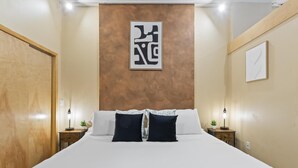 A hotel room with a large bed, two bedside tables with lamps, a wall-mounted artwork, and a wooden door. - European Village King Suite Retreat: Unwind, Explore, Beach, Work! (Palm Coast)