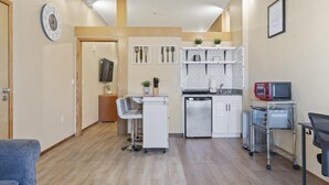 A compact kitchen with white cabinets, a microwave, a dishwasher, and a small bar area with a chair and cart. - European Village King Suite Retreat: Unwind, Explore, Beach, Work! (Palm Coast)
