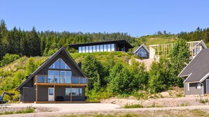 En modern stuga med en stor glasfasad, belägen på en sluttning med en skog som bakgrund.