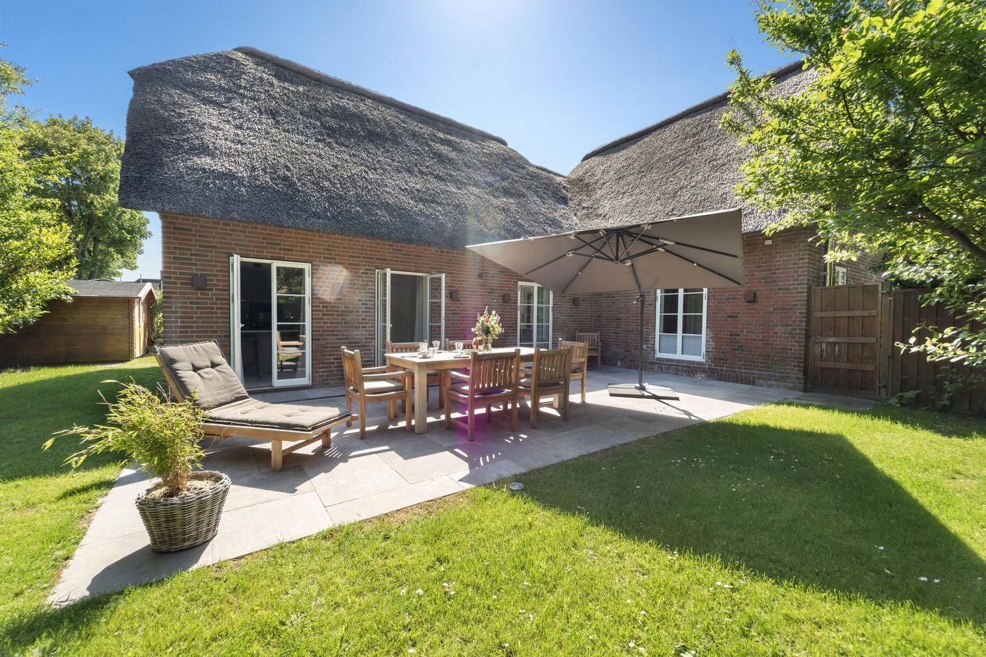 A patio area with a table and chairs, a thatched roof, and a brick building.