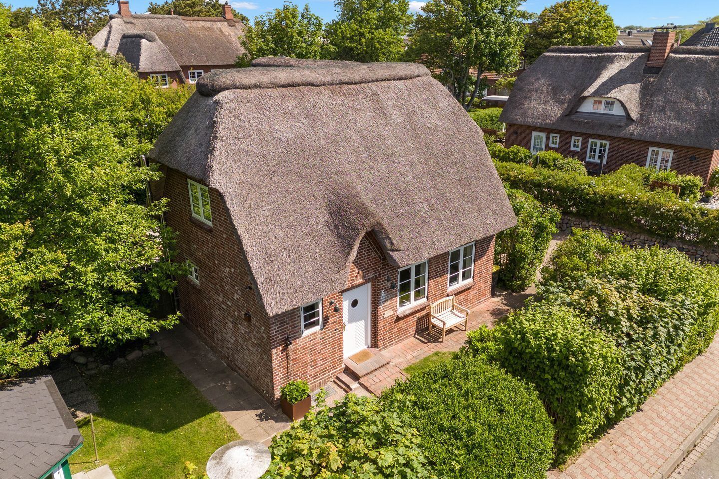 A brick house with a thatched roof, a small front porch, and a well-maintained garden.