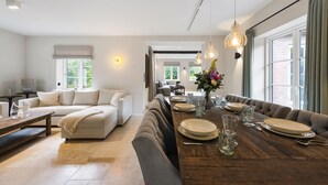 Una sala de estar moderna con comedor, que presenta una mesa de madera para seis comensales, un sofá y un ventanal que proporciona luz natural.