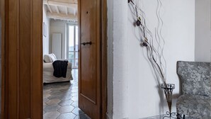 A room with a wooden door, a sofa, a patterned armchair, and a wall-mounted decorative piece. - GuestHost - Bright apartment perfect for 4 people, with 2 bedrooms and 2 bathrooms, located in a period building in the heart of the historic center (ZTL). The apartment boasts all the main comforts, including a private garden, an oasis of peace and gree (Perugia)