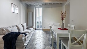 A modern living room with a sofa, a dining table with chairs, a vase with dried flowers, and a hexagonal patterned floor. - GuestHost - Bright apartment perfect for 4 people, with 2 bedrooms and 2 bathrooms, located in a period building in the heart of the historic center (ZTL). The apartment boasts all the main comforts, including a private garden, an oasis of peace and gree (Perugia)