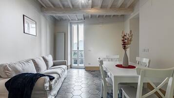 Ein modernes Wohnzimmer mit einer Couch, einem Esstisch mit Stühlen, einer Vase mit Trockenblumen und einem sechseckig gemusterten Boden.