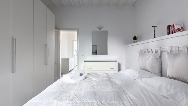 A bedroom with a bed, a dresser, a mirror, and a wardrobe. - GuestHost - Bright apartment perfect for 4 people, with 2 bedrooms and 2 bathrooms, located in a period building in the heart of the historic center (ZTL). The apartment boasts all the main comforts, including a private garden, an oasis of peace and gree (Perugia)