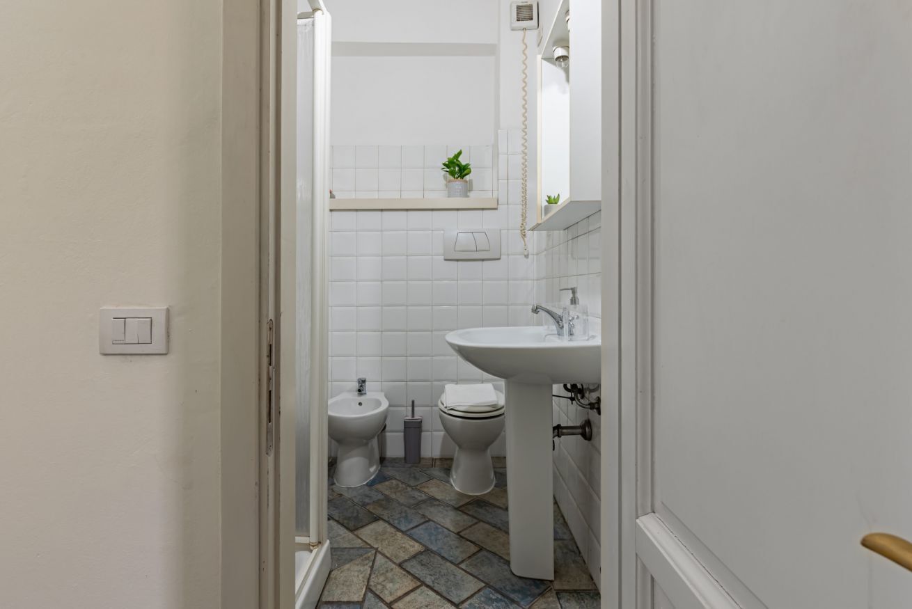 Une salle de bain avec un lavabo blanc, deux toilettes, un bidet et une petite étagère sur laquelle est posée une plante.