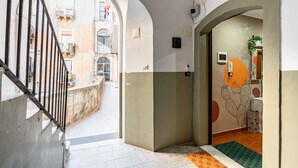 A narrow hallway with a tiled floor, a metal railing on the left, and a door with a cactus mural on the right.