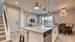 Une cuisine spacieuse avec un grand îlot central, un coin repas avec une table et des chaises, un escalier et un lustre.