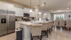 Una cocina moderna con electrodomésticos de acero inoxidable, una isla central con taburetes altos y luces colgantes.