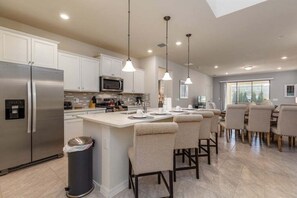 A modern kitchen with stainless steel appliances, a central island with bar stools, pendant lighting, and a dining area with a large window.