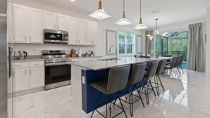 A modern kitchen with white cabinets, stainless steel appliances, and a central island with bar stools. - Stunning Modern Home! (Kissimmee)