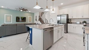 A modern kitchen with a central island, white cabinets, stainless steel appliances, and pendant lighting. - Stunning Modern Home! (Kissimmee)