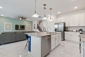 A modern kitchen with a central island, white cabinets, stainless steel appliances, and pendant lighting.